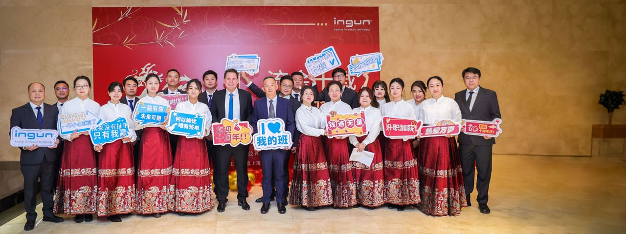 Festive group photo of INGUN employees from China in festive attire and holding paper signs with congratulations in their hands